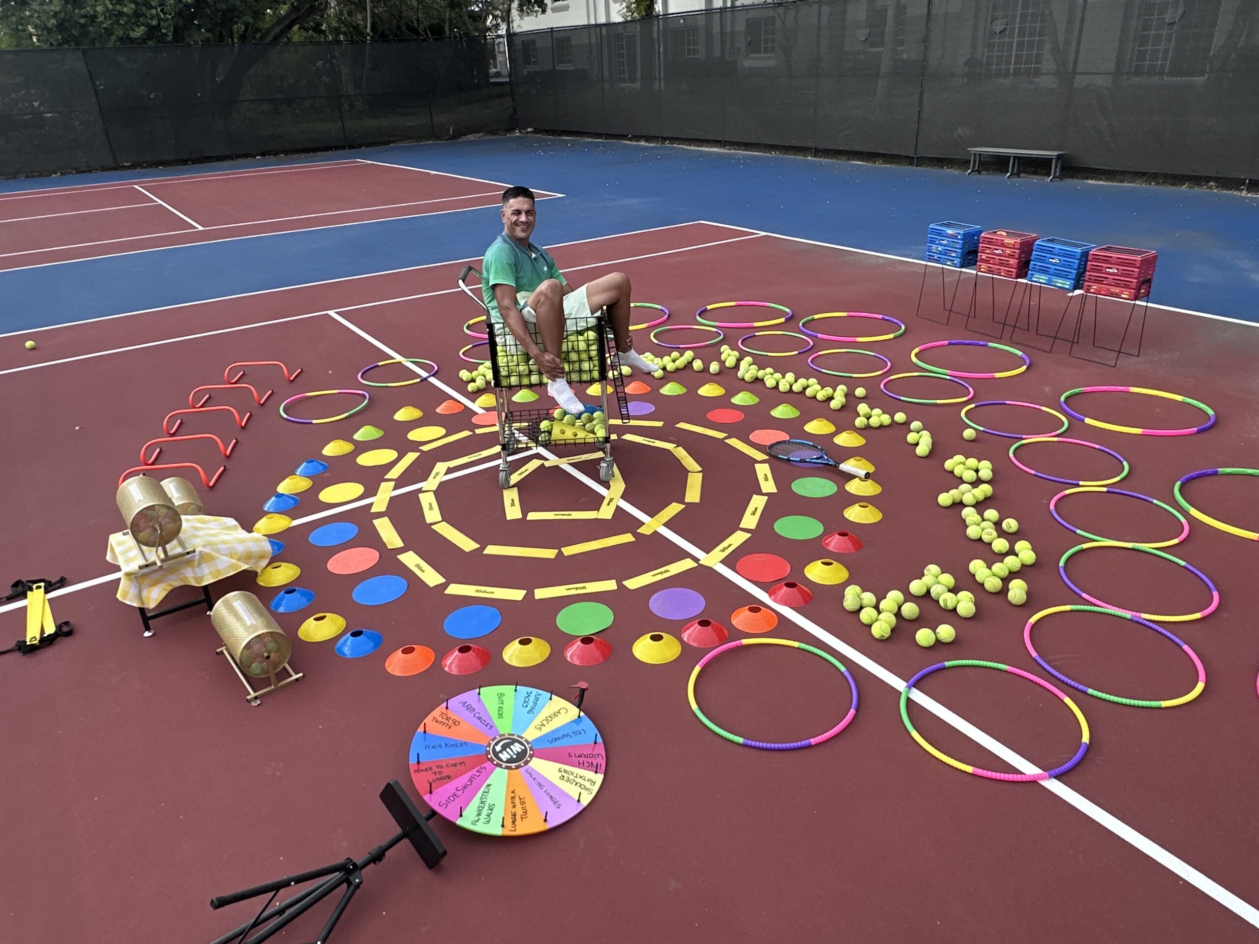 Jackson Phillips seated in a ball cart surrounded by a spiral of hoops, cones and tennis balls set up for a themed cardio tennis clinic in Fort Lauderdale