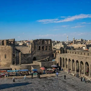 advanced cardio tennis classes — the black basalt streets and colonnades of ancient Bosra under a hard southern Syrian sun, the citadel walls rising behind them.