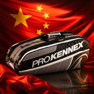 beginner cardio tennis lessons Fort Lauderdale — the Prokennex Q Gear Tennis Bag (12 Racquet) and the flag of the People's Republic of China combined by the model into a single photoreal composition. The red field fills the frame in deep side-lit folds with the one large gold star and the arc of four smaller stars in the upper hoist, and the grey and black bag is composed into the arrangement so its long horizontal line runs beneath the stars and the fold of the cloth wraps its end, with no lettering anywhere in the picture.
