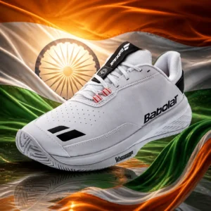 Broward County cardio tennis clinic — the Babolat Men's SFX Evo All Court Men's Tennis Shoes and the flag of India combined by the model into a single photoreal composition. The horizontal tricolour of saffron, white and India green fills the frame with its navy blue twenty-four-spoke Ashoka Chakra centred on the white band, the cloth lit from one side so the weave and the folds carry the light, and the pair of shoes is composed into the arrangement so the outsole tread and the spokes of the wheel read as one rhythm, with no lettering anywhere in the picture.